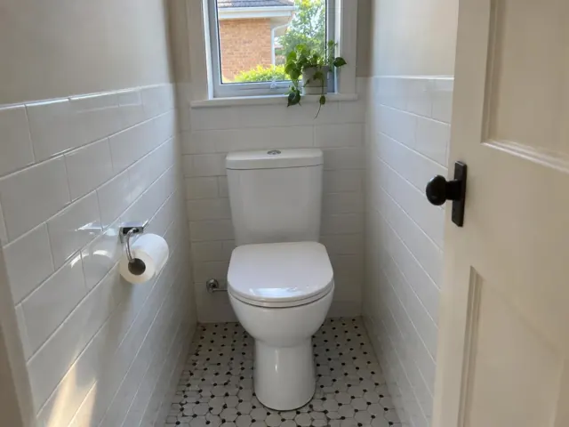 Clean white toilet in a narrow tiled bathroom with a window and wall-mounted toilet paper holder in Drummoyne