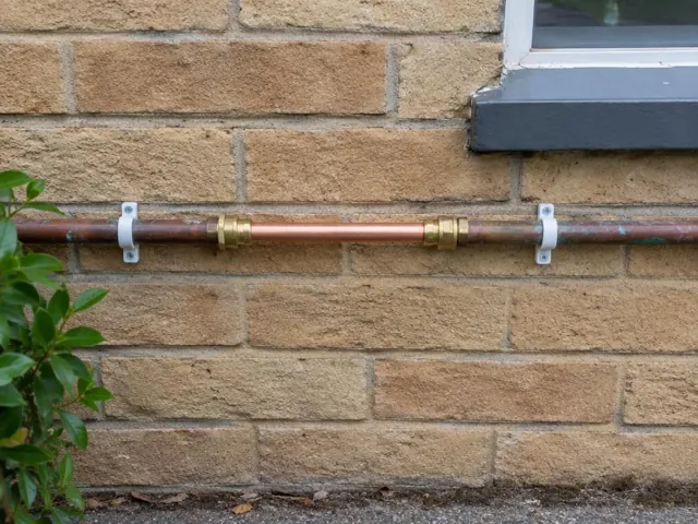 Repaired copper water pipe on a brick exterior wall near a window in Abbotsford