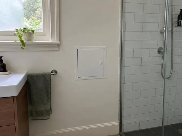 Bathroom wall with a small access panel beside a vanity and shower in a tiled room in Cabarita